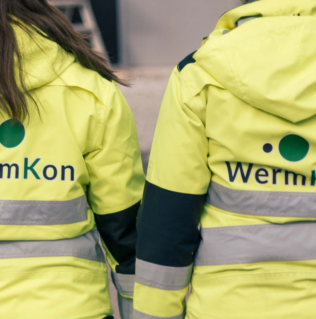 ryggarna på två varselklädda personer, på ryggen är det en wermkon-logga
